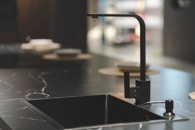 Pürüzsüz ve modern mutfak lavabosu ve musluğu karanlık bir dolabın ve mermer bir tezgahın üzerine kurulmuş. Musluk, uzun, kemerli ve siyah kaplamalı tek kollu bir tasarım..