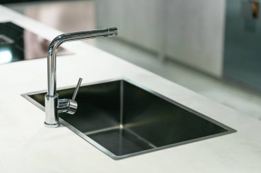 Pürüzsüz ve modern mutfak lavabosu ve musluğu karanlık bir dolabın ve mermer bir tezgahın üzerine kurulmuş. Musluk, uzun, kemerli ve siyah kaplamalı tek kollu bir tasarım..