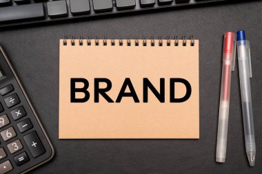 Defterde hesap makinesi ve ofis malzemeleriyle Brand metni var. Markanı yap. Marka oluşturma, başarı, iş.