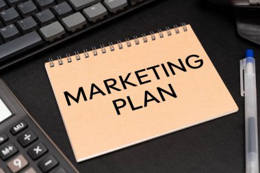 Not Defteri 'nde hesap makinesi ve ofis malzemeleriyle işaretlenmiş plan metni. Pazarlama Planı İş Reklamcılığı.