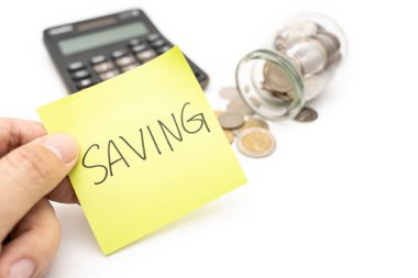 Beyaz arka planda izole edilmiş cam para kavanozuna yapışkan not, hesap makinesi ve madeni paralar içeren metin kaydediliyor. Para biriktirme kavramı.