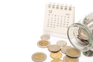 2025 ARALIK Tay Baht Bozukluklarıyla dolu takvim beyaz zemin üzerine izole edilmiş kavanoz bardaktan döküldü, gelecek için tasarruf, yatırım iş konsepti. Boşluğu Kopyala.