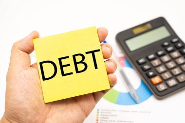 Hesap makinesiyle yapışkan notla ilgili DEBT metni. Ekonomik kriz riski ve sorun konsepti. Mali borç azalması, gelir yönetimi kavramı.