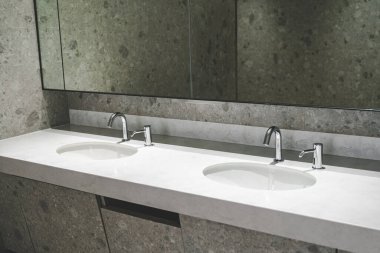 Temiz umumi tuvalette modern krom otomatik musluk ve sabun dağıtıcısı. Beyaz seramik leğende krom su musluğu.