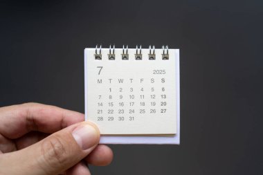 Temmuz 2025 arka planı için El Tutma Masası Takvimi. Koyu arkaplanda 2025 JUL takvimi olan takvim kavramı.