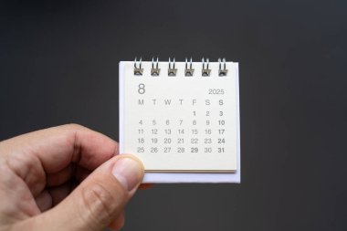 AĞUSTOS 2025 arka planı için El Tutma Masası Takvimi. Koyu arkaplanda 2025 AUG takvimi olan takvim kavramı.