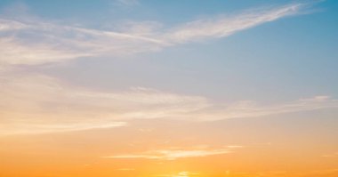 Gün batımında ince bulutlu, sakin, pastel gökyüzü, mavi, turuncu ve sarı renklerin nazik bir gradyanı sergiliyor..