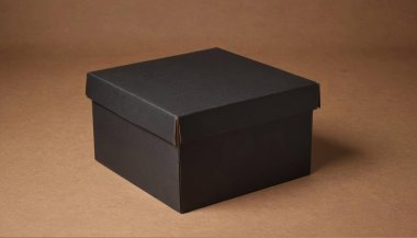 Kapalı kare siyah karton kutu kahverengi bir yüzeyde duruyor. Zarif ve temiz karton kutu ürünü için kaliteli fotoğraf modeli.