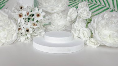 Minimalist ürün sergisi beyaz çiçeklerle çevrili iki katmanlı yuvarlak bir platform içeriyor. Afişler ve posterler için güzel ve yumuşak renk tonlarına sahip modern fotoğraflar.