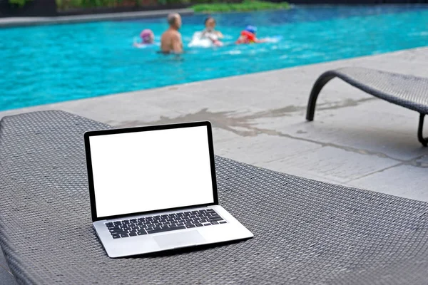 Laptop with blank screen for creative design on sunbed nearby swimming pool background. Computer notebook with monitor clipping path for present landing page design. Laptop computer mock up template