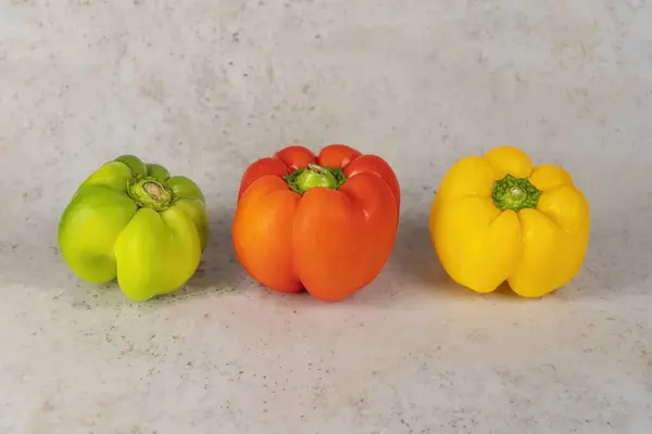 Üç parça biber, yeşil, turuncu ve kırmızı açık gri mermer arka planda izole edilmiş.