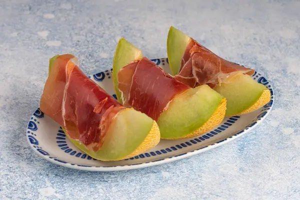 Kavun ve Serrano jambonu, beyaz arka planda izole edilmiş, süslenmiş bir porselen tabakta dilimler.