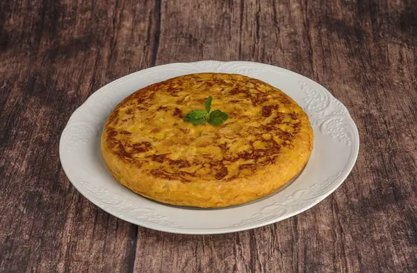 Kırsal bir masada beyaz bir tabakta patates ve soğanlı omlet.