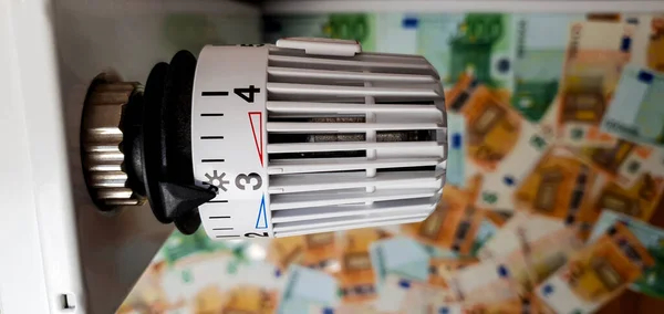 Close-up of the temperature regulator of the heating radiator battery against the background of banknotes of 50 and 100 euros. The concept of rising heating costs in the winter cold period. Rise in energy prices, energy crisis and recession