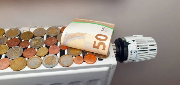 The concept of the high cost of heating and electricity and the impending energy crisis. On a heating radiator with a thermostat, a pack of 50 euro banknotes and a lot of coins of different denominations