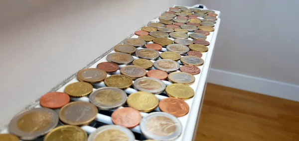 The concept of the high cost of heating and the need to save money during the cold season. There are a lot of coins on a heating radiator with a thermostat