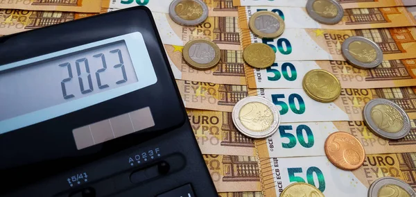 stock image 2023 financial year. Calculator on the background of euro bills and coins. Number 2023 on the calculator screen