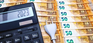 Hesap makinesinin yanındaki elektrik prizi çok sayıda banknotun arka planında. 2023 yılında yüksek elektrik, enflasyon ve kriz maliyeti kavramı