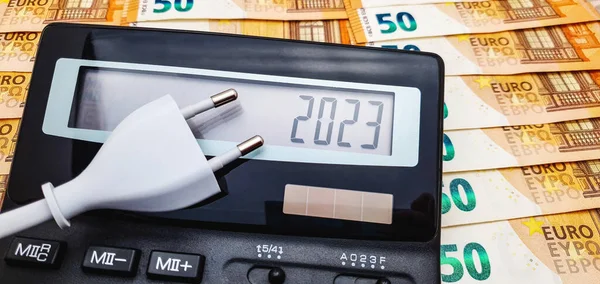 Çok sayıda 50 avroluk banknotun arka planında elektrik prizi ve hesap makinesi var. 2023 yılında yüksek elektrik, enflasyon ve kriz maliyeti kavramı