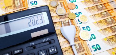 Arkaplanda para ve hesap makinesi ve elektrik prizi var. 2023 yılında yüksek elektrik maliyeti, yükselen enflasyon ve yaklaşan kriz kavramı