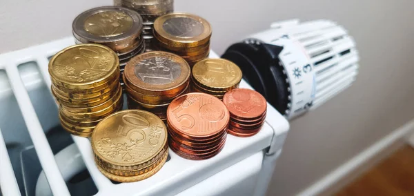High heating costs and the need for savings in the cold season. There are a lot of coins on the heating batteries. Heating battery thermostat in the background