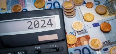 Avrupa 'da yeni mali yıl 2024. Yaşam, enerji, gıda ve malların sürekli artan maliyeti. Hesap makinesi, Avro banknotlarının arka planında bir sürü bozuk para