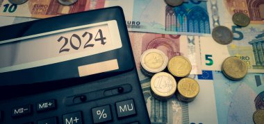 2024 yılında Avrupa 'yı enerji ve mali kriz sardı. Enerji, gıda ve malların artan maliyetleri sorun yaratıyor. Avro paralarının ve banknotların arasında hesap makinesi