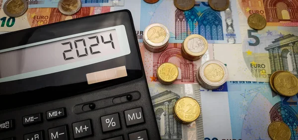 2024 yılında Avro için parlak bir gelecek. Bol miktarda para, bozuk para ve hesap makinesi finansal büyümeyi sembolize eder. Hesap makinesi ekranında, ekonomik iyimserliği yansıtan 2024 yılı gösteriliyor