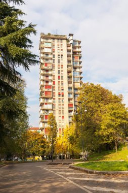 One multi-story residential building in the city among green trees against a light blue sky background
