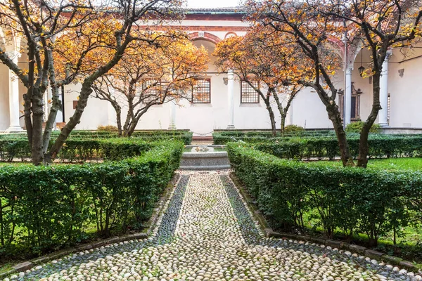 The courtyard garden of the building with trees and bushes in the form of a circle in green and a small stone path between them