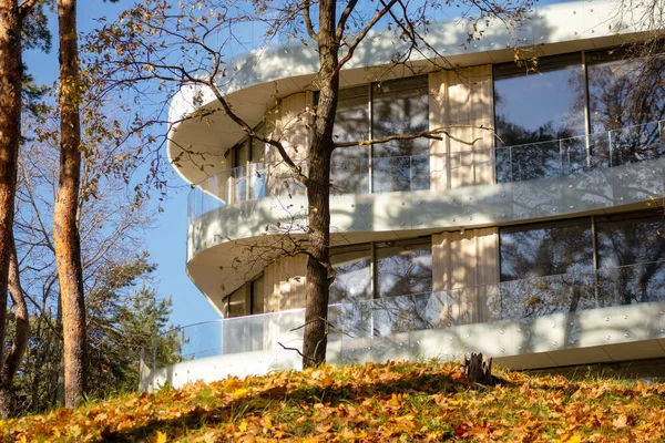 Sonbahar ağaçlarının arasından manzaralı, deniz kenarında camlı pencereleri olan modern bir bina.