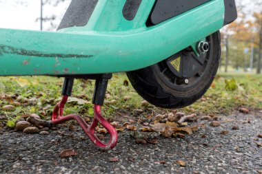 Duruş pozisyonunda bacağının üzerine yeşil bir motosiklet yerleştirilmiş.