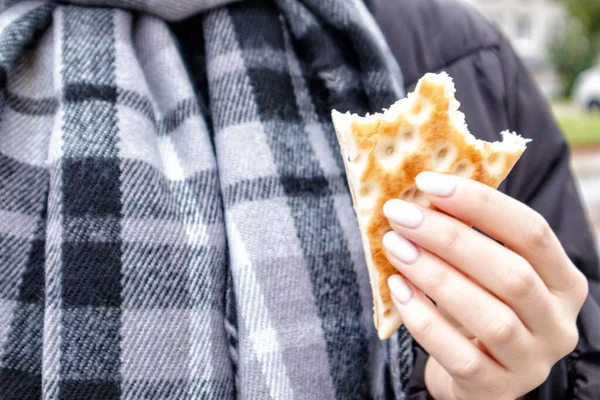 Hands with white nails and a bite of breakfast bread on a background of a gray checkered scarf