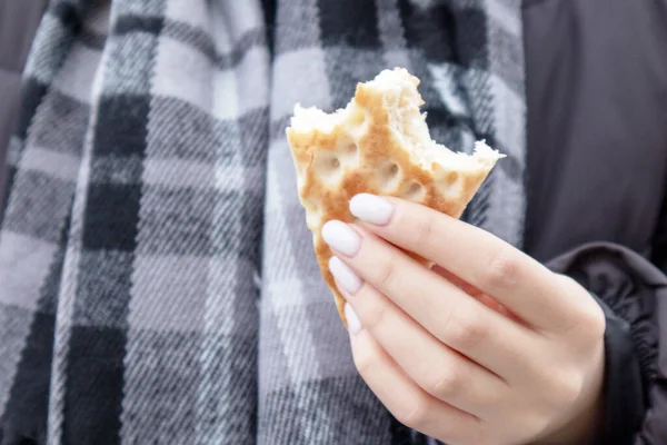 Hands with white nails and a bite of breakfast bread on a background of a gray checkered scarf