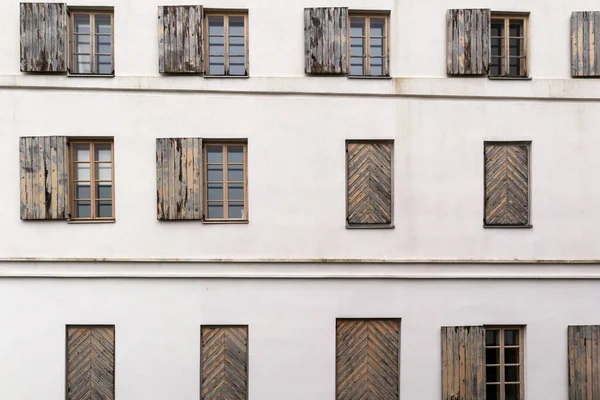 A white building wall with many horizontal windows and wooden shutters on it