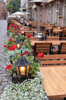 Dışarıdaki teras kafede kırmızı çiçekler ve bir lamba.