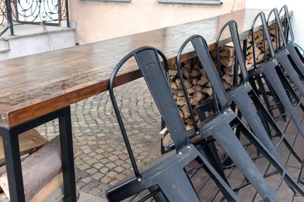 A wooden table with a row of padded chairs on it in an outdoor c