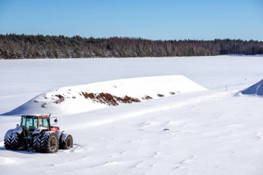 Kışın, ağaç ve mavi arka planlı kırmızı büyük traktör sahada.