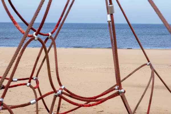 Red rope sections fastened with a metal clamp on a background of brown sand and blue sea