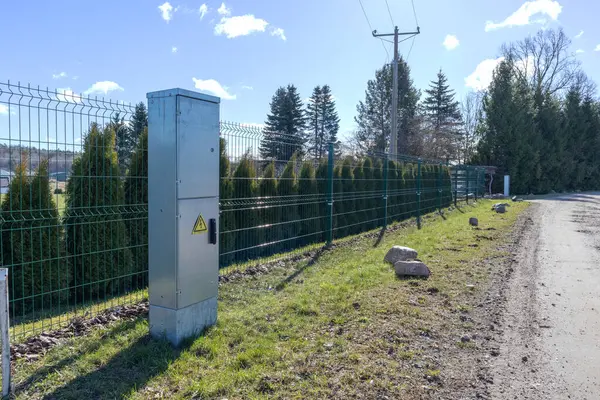 Metal electrical distribution box in front of the fence