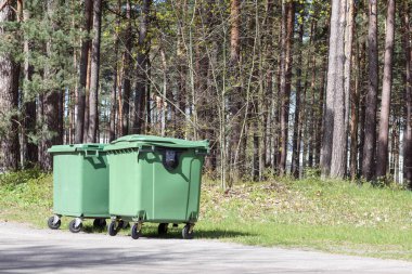 Ormanın arka planındaki parkta yeşil renkli çöp tenekeleri