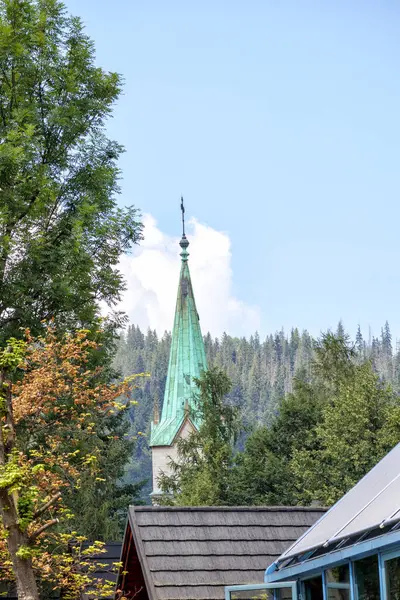 Dağlarda ağaç dalları arasında yeşil kilise kulesi