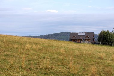Dağlarda doğal bir manzara eğimli bir dağ çayırı ve üzerinde bir ev var.