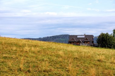 Dağlarda doğal bir manzara eğimli bir dağ çayırı ve üzerinde bir ev var.