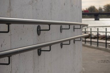 Metal parmaklıkları olan beton bir duvar parçası. Tırabzan, duvara metal bağlayıcılarla tutturulmuş iki paralel boru sapından oluşuyor. Sapları siyaha boyanmış..