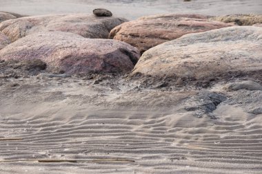 Kumlu bir sahilde, rüzgarın etkisi altında ilginç çizgiler oluşturan birkaç büyük yuvarlak taş..