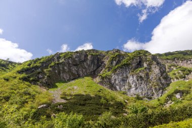 Bir patika boyunca esen kayalık duvarları olan dik bir dağ yamacı. Ama yamacın alt kısmı yeşil bitki örtüsüyle kaplı..