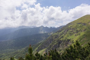 Yeşil yamaçları uzak dağ tepelerine kadar uzanan tepe manzarası kısmen bulutlarla kaplı..
