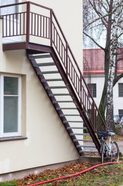 An iron staircase structure on the wall of a building leading to a balcony with a bicycle parked next to it. clipart