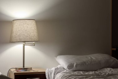 İki beyaz yastıkla boş bir yatağı aydınlatan bir masa başı lambası..